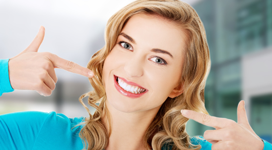smiling broadly woman pointing at her perfect teeth