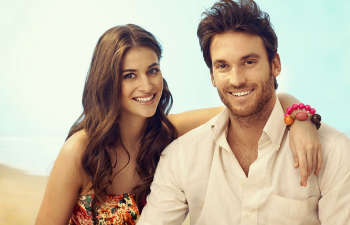 A young man and woman posing for a photo on the beach.