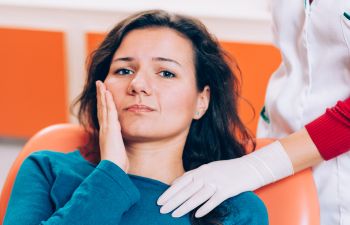 A woman with dental pain sitting in a dentist's chair.