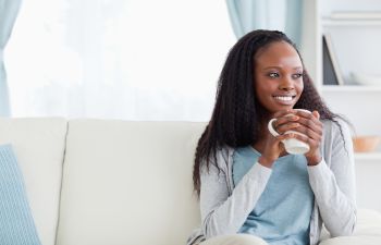 A young african american woman sitting on a couch holding a coffee mug.