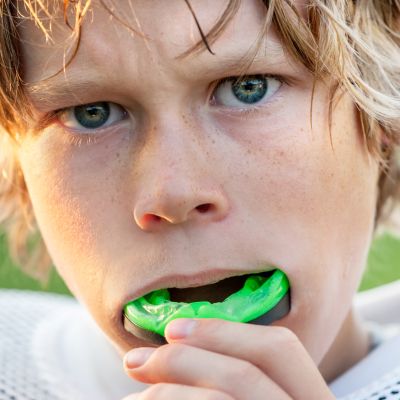 A young athlete boy inserting a green mouthguard before the match