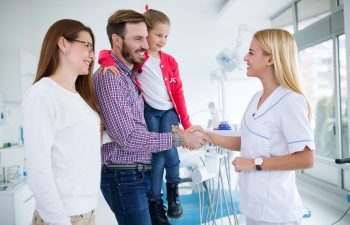 a dentist welcoming parents with a little daughter at the first visit to her dental office
